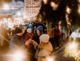 Eine Personengruppe steht zum Weihnachtsmarkt auf dem Marktplatz in Wernigerode unter dem Weihnachtsbaum und trinkt Glühwein.