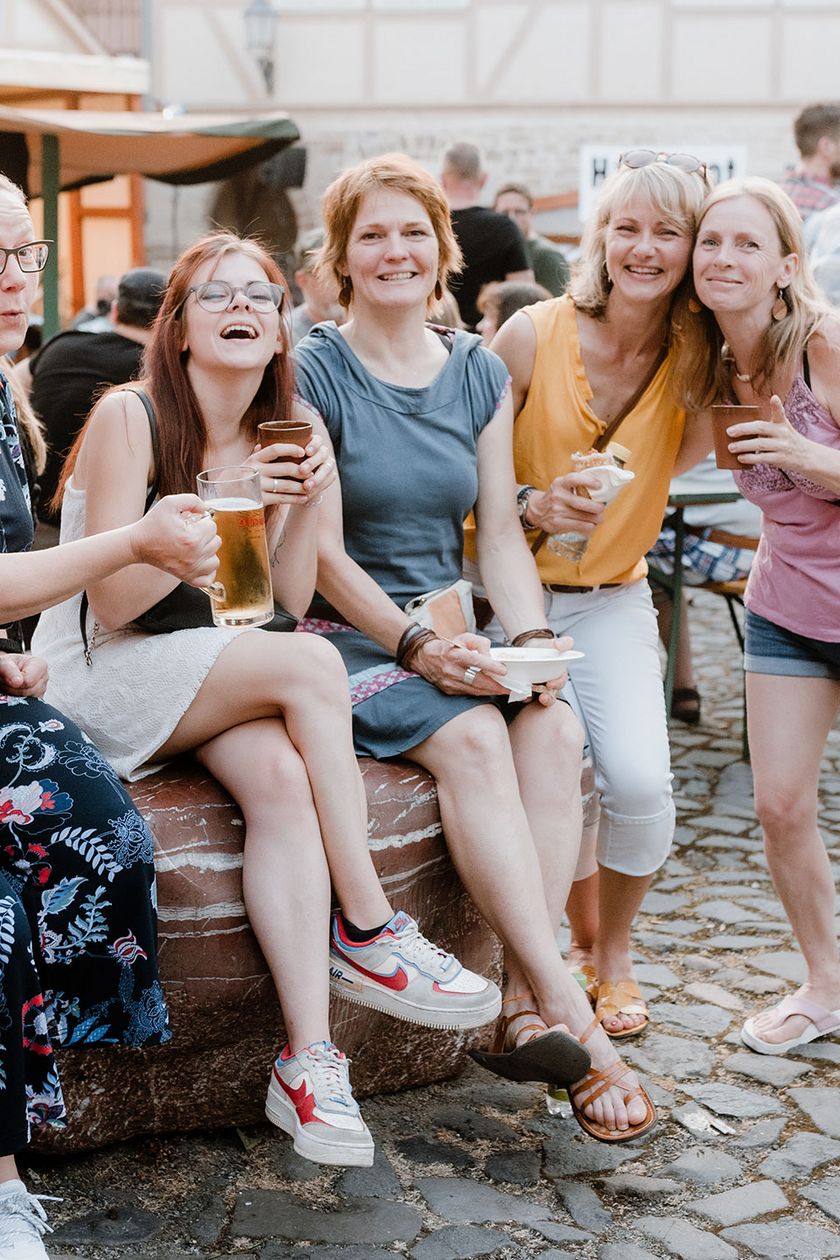 Eine Gruppe von Personen sitzt auf dem Mittelaltermarkt zum Rathausfest in Wernigerode auf einer Mauer und unterhalten sich.