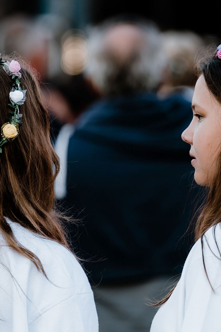 Zwei Personen mit Blumenkränzen stehen mit dem Rücken zur Kamera