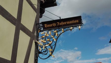 Der Ausleger mit dem Hinweis zum Eingang der Tourist-Information strahlt im Gegenlicht des blauen Himmels.