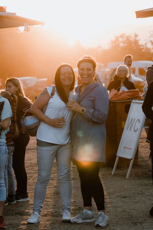 Besucher des MDR Harz Open Air stehen vor einem Gastronomiestand im Gegenlicht auf der Zaunwiese im Bürgerpark Wernigerode.
