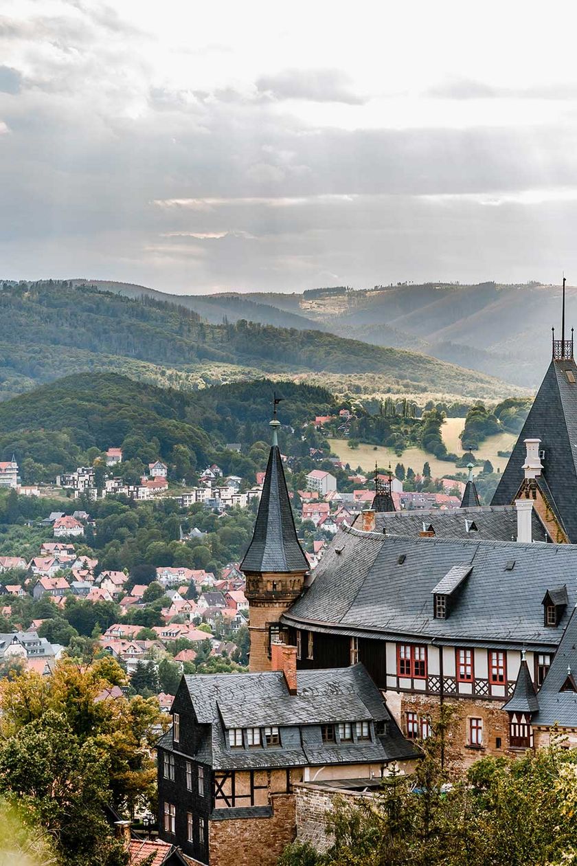 Der Blick geht vom Agnesberg zum Schloss Wernigerode mit der Stadt und den Bergen des Harzes im Hintergrund.