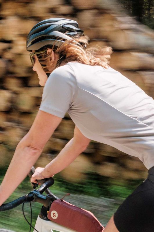 Eine Teilnehmerin am Gravel Bike Fest in Schierke fährt auf dem Fahrrad an einem Holzstapel vorbei.
