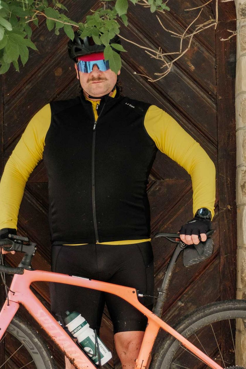 Ein Radfahrer steht unter einem Baum an eine Tür angelehnt.