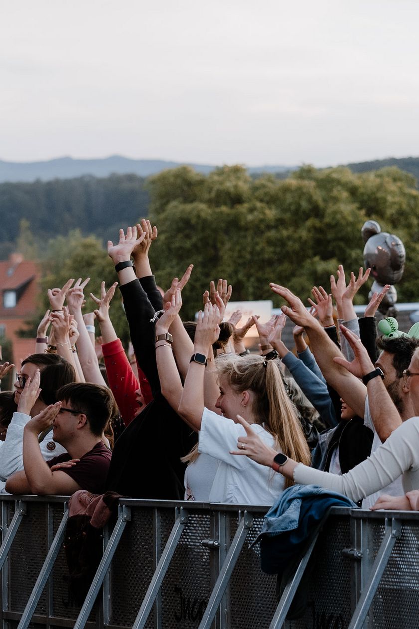 Besucher des MDR Harz Open Air stehen vor einer Bühne und jubeln mit erhobenen Armen.