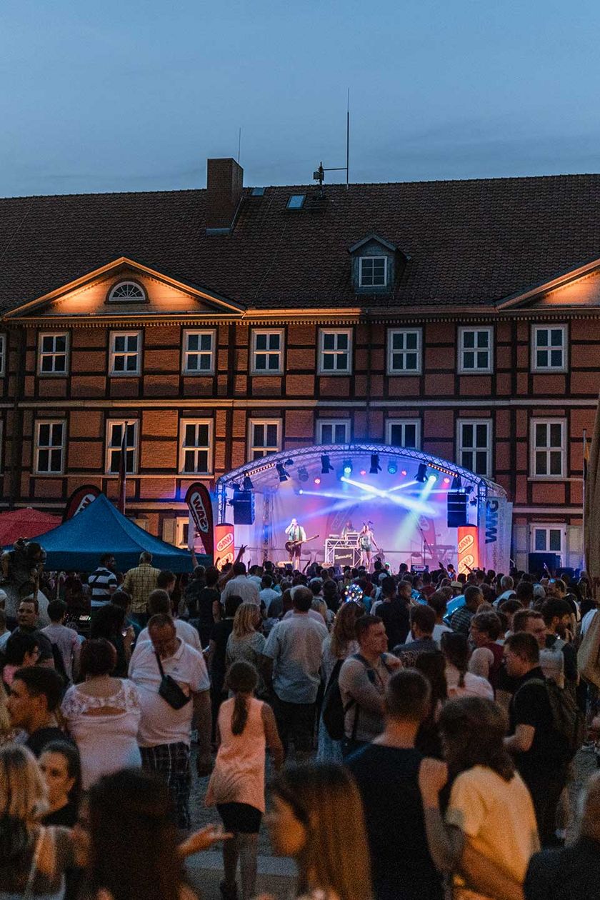 Publikum steht vor einer Bühne in abendlicher Stimmung zum Rathausfest auf dem Nicolaiplatz in Wernigerode.
