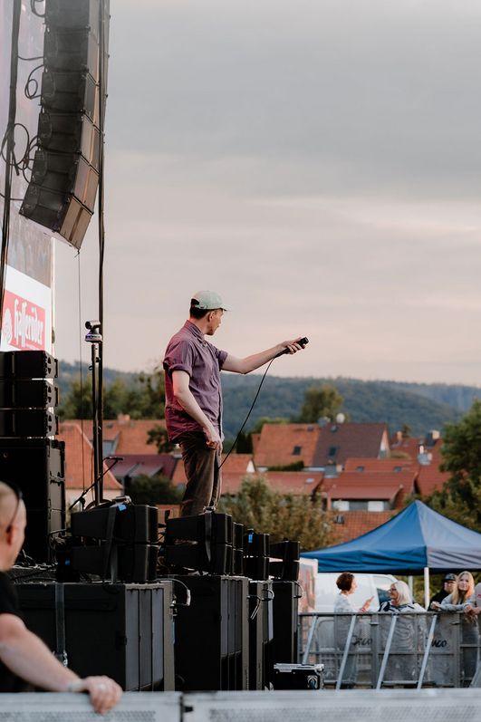 Ein Sänger steht auf der Bühne des MDR Harz Open Airs in Wernigerode. Vor Ihm das Publikum und hinter ihm sind die Berge des Harzes zu erkennen.